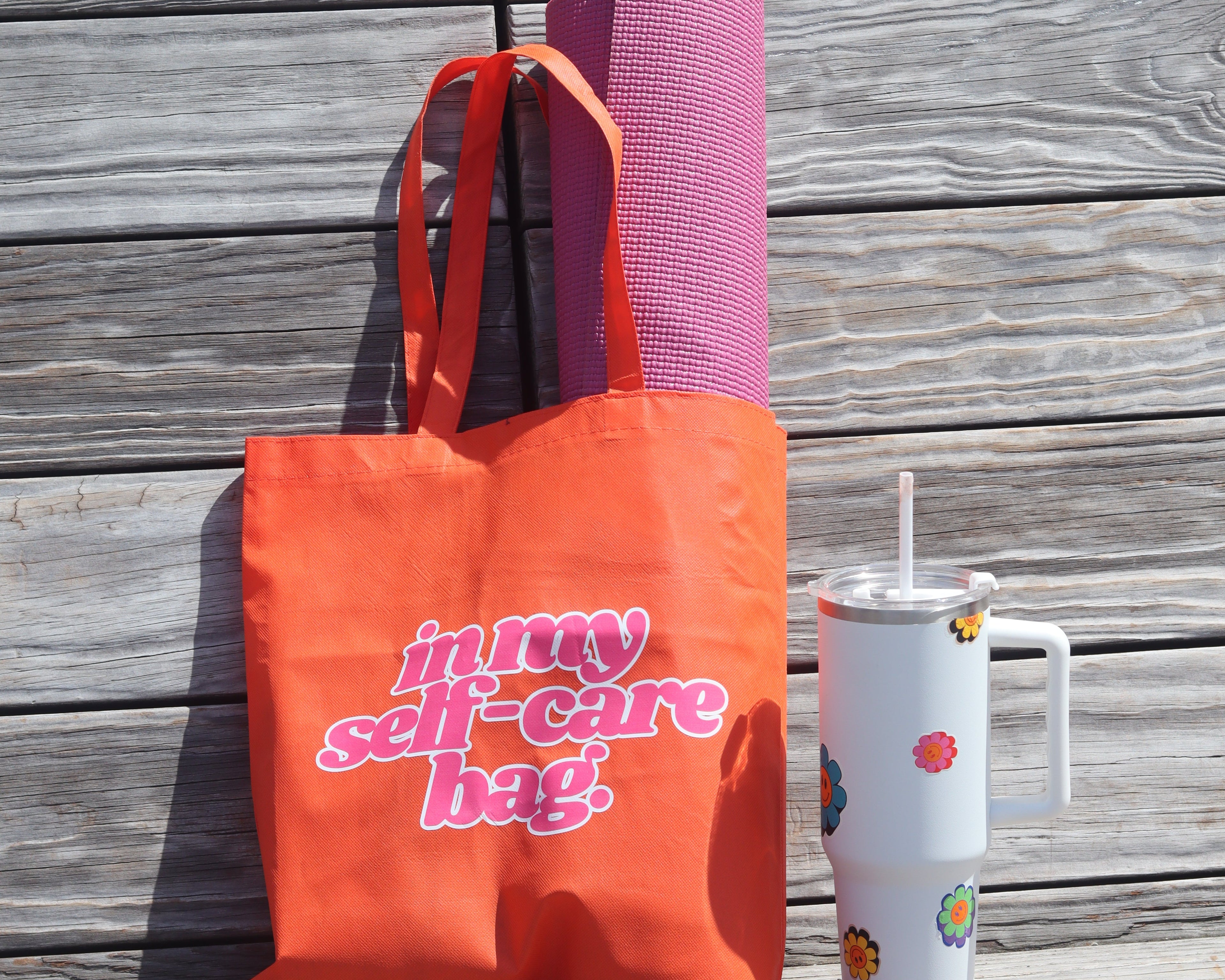 Orange tote bag with pink text on a wooden surface